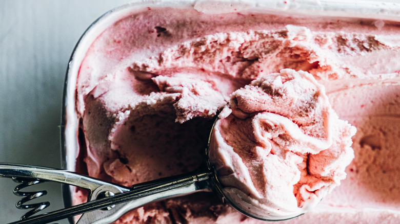 scooping strawberry ice cream from tub